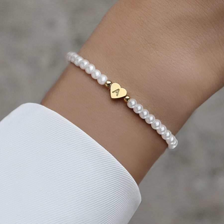 Een minimalistische en elegante parelarmband met een gouden hartvormige hanger gegraveerd met de letter "M". Deze Double Love Heart Bracelet straalt tijdloze klasse en verfijning uit, perfect voor een persoonlijke en stijlvolle toevoeging aan elke outfit.