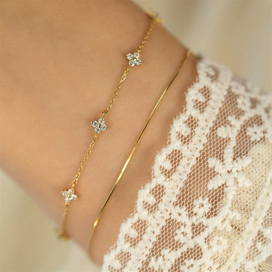 Een verfijnde close-up van de Perle Épure armband met delicate gouden schakels en subtiele bloemvormige accenten, ideaal voor een minimalistische en tijdloze elegantie